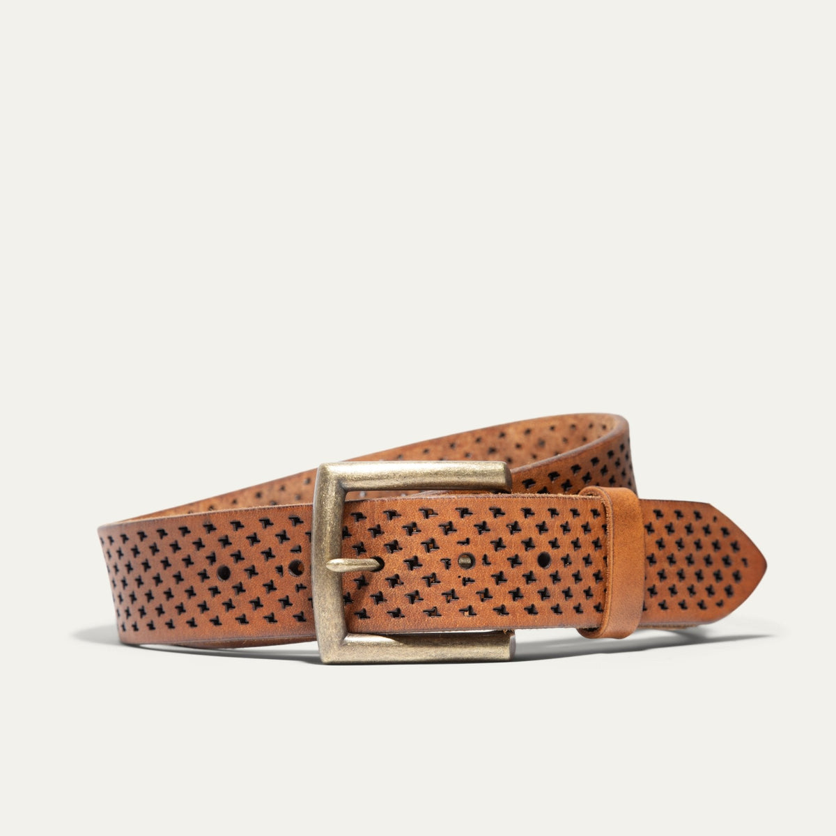 Tan leather belt coiled flat, showing the full star-perforated laser-cut pattern and antique brass buckle