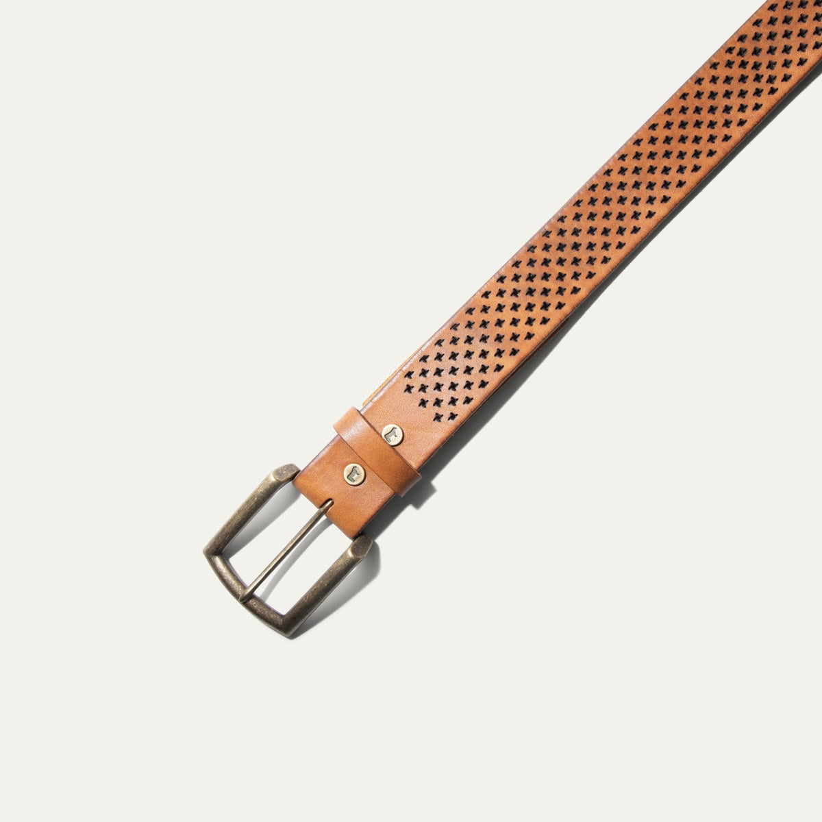 Close-up angled view of the tan leather belt showing the antique brass buckle and star-shaped perforated pattern