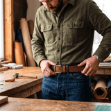 Man in an olive work shirt and jeans wearing the tan star-perforated leather belt in a woodworking studio