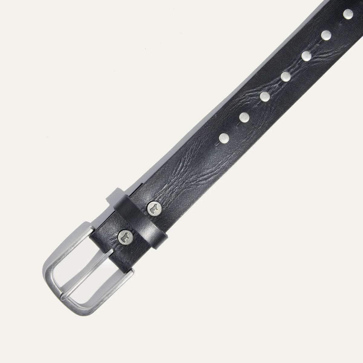 Close-up of the Will Leather Goods Single Studded Belt in black leather, showing the brushed silver buckle, keeper loop with embossed dog logo, and stud rivets.
