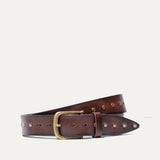Will Leather Goods Single Studded Belt in brown leather, coiled flat showing the row of antique brass stud rivets along the edge and the brass buckle, on a white background.