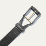 Close-up of the black leather buckle belt's brass roller buckle and keeper loop, on a white background.