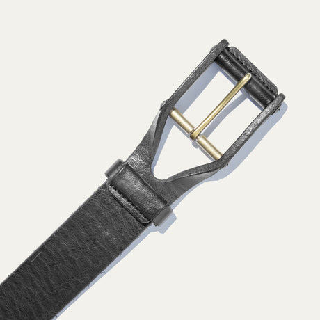 Close-up of the black leather buckle belt's brass roller buckle and keeper loop, on a white background.