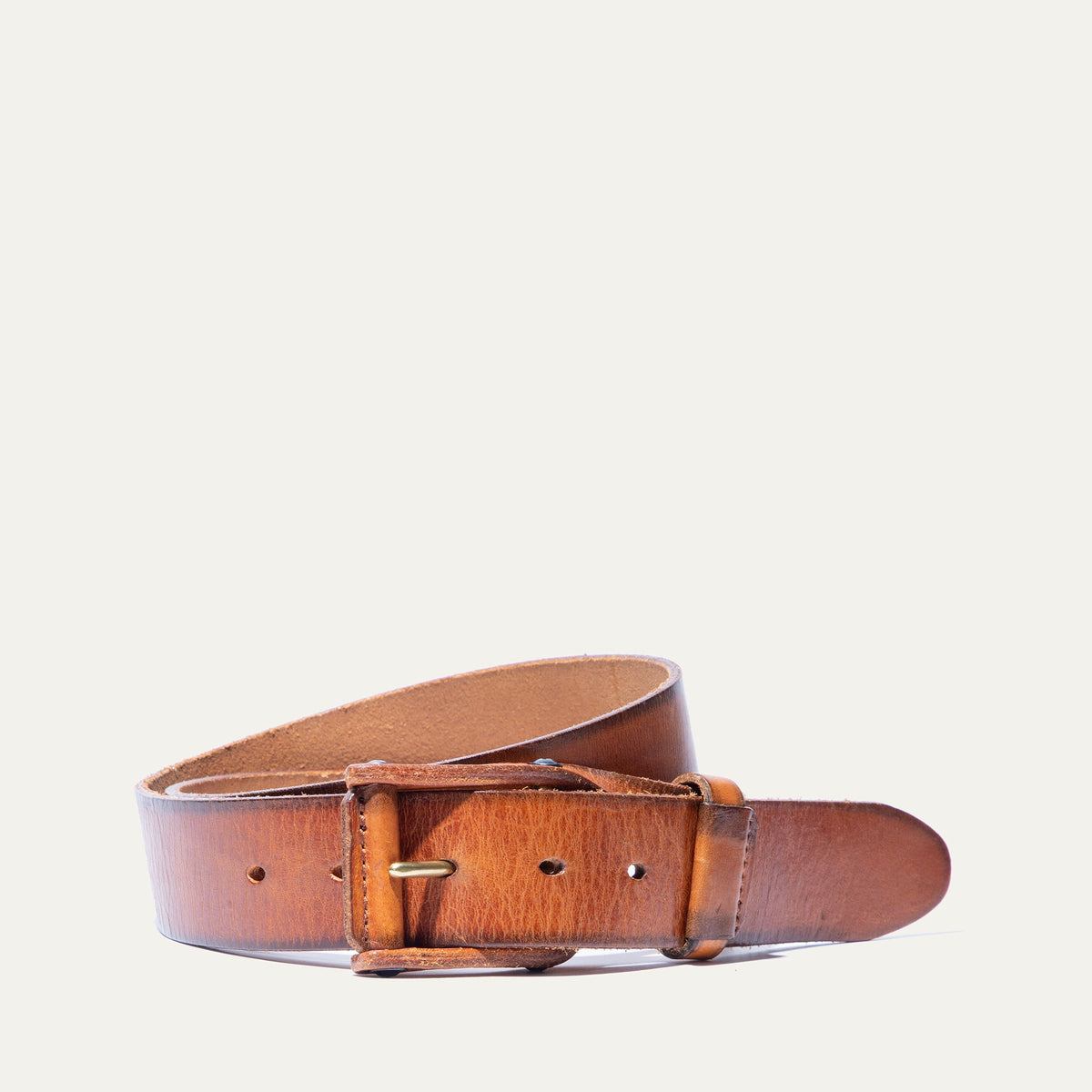 Will Leather Goods Leather Buckle Belt in tan/cognac leather, coiled side view showing the brass roller buckle, on a white background.