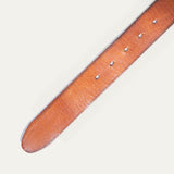 Close-up of the tan leather buckle belt strap showing natural grain texture and the row of metal-grommeted buckle holes.