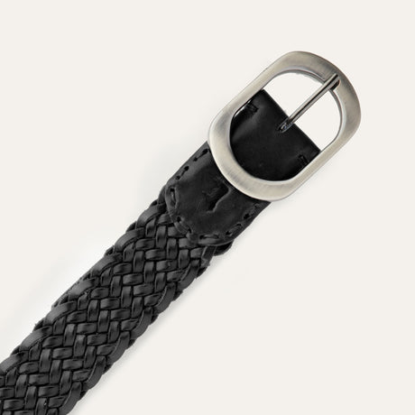 Close-up of the black Twelve Strand Braided Belt's brushed silver oval buckle and keeper loop, showing the embossed Will Leather Goods dog logo and twelve-strand braid detail.