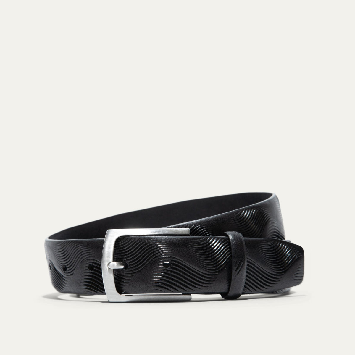 Will Leather Goods Wave Embossed Belt in black, coiled flat showing the wave-textured embossed leather and brushed silver buckle, on a white background.