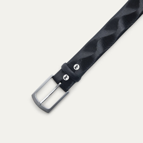 Close-up of the Will Leather Goods Wave Embossed Belt in black, showing the brushed silver buckle, keeper loop with embossed dog logo snap, and wave-textured leather.