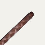Close-up of the Will Leather Goods Wave Embossed Belt strap tip in cognac brown, showing the wave-textured embossing and adjustment holes with silver grommets.
