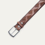 Close-up of the Will Leather Goods Wave Embossed Belt in cognac brown, showing the brushed silver buckle, keeper loop with embossed dog logo snap, and wave-textured leather.