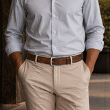 Lifestyle photo of a man in a light blue shirt and beige pants wearing the Will Leather Goods Wave Embossed Belt in cognac brown with a silver buckle, hands in pockets.