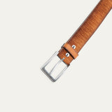 Close-up of the Wood Grain Embossed Belt's brushed silver buckle and keeper loop, showing the wood-grain embossed tan leather texture and a small Will Leather Goods dog logo stud.