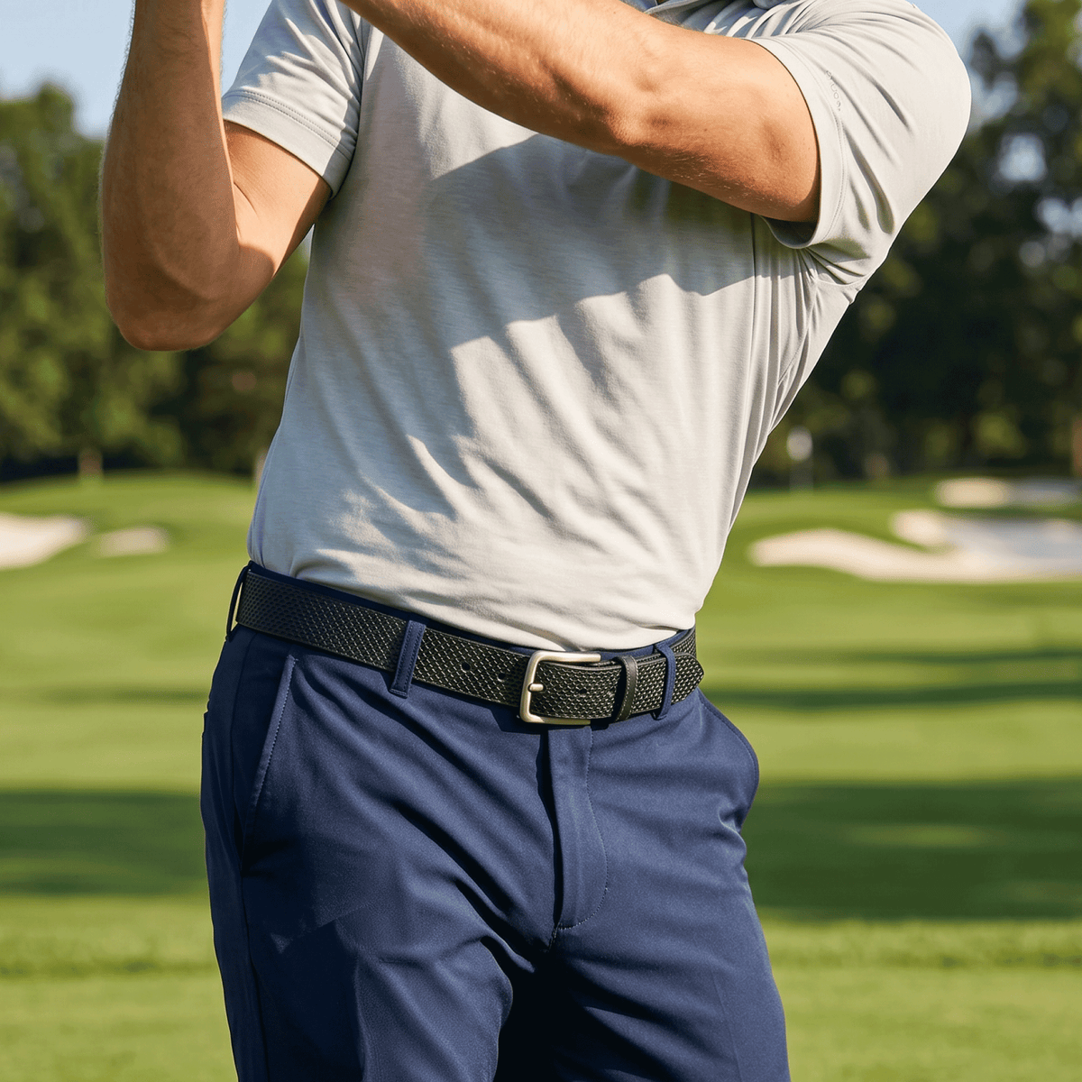 Man wearing the black diamond-embossed belt with navy golf trousers and a gray polo on a golf course.