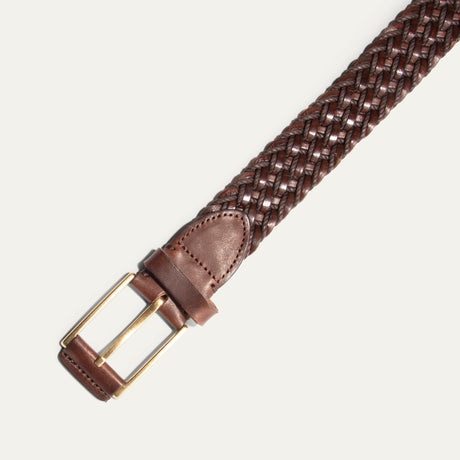 Close-up diagonal view of the dark brown braided belt's buckle end, showing the brushed nickel buckle and leather keeper loop