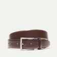 Will Leather Goods Glazed Calfskin Belt in cognac brown, coiled flat showing the polished leather strap, brushed silver prong buckle, and keeper loop, on a white background.