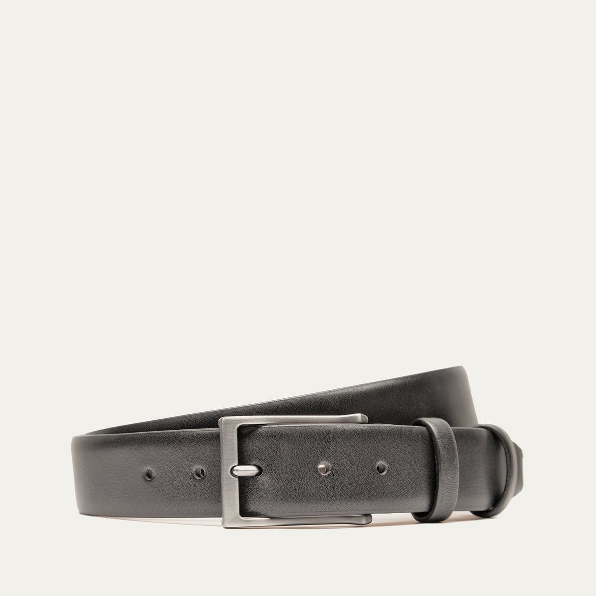 Will Leather Goods Glazed Calfskin Belt in black, coiled flat showing the polished leather strap, brushed silver prong buckle, and keeper loop, on a white background.