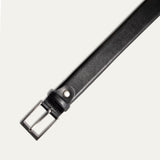 Close-up of the Will Leather Goods Glazed Calfskin Belt in black, showing the brushed silver buckle attachment, keeper loop, and rivet detail against a white background.