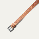 Close-up of the Hand-Tooled Morning Glory Jean Belt buckle in natural tan leather, showing the hand-tooled floral scrollwork and antique nickel roller buckle.