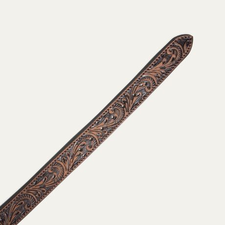 Close-up of the Hand-Tooled Morning Glory Jean Belt buckle in antiqued brown leather, showing the hand-tooled floral scrollwork and antique nickel roller buckle.