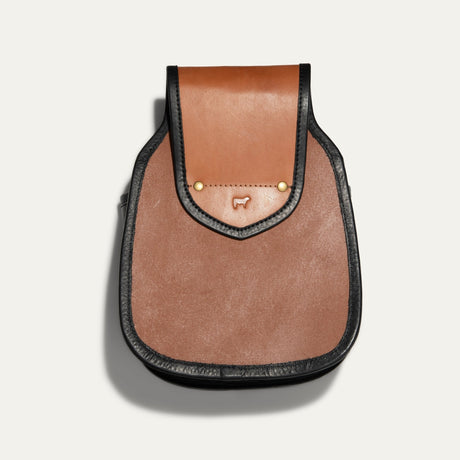 Will Leather Goods Ammo Belt Bag in cognac leather, front view with flap closed over two brass snap studs and embossed cow logo, black trim, on a white background.