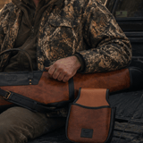 Lifestyle photo of a hunter in camo sitting in a truck bed, cognac leather Ammo Belt Bag and matching Will Leather Goods gun case and duffle resting beside him.