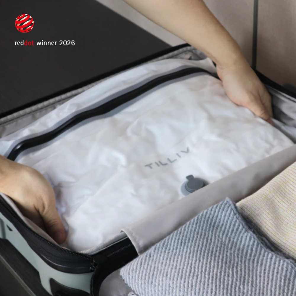 Hands settling a white TILLIV Compak Medium full of folded clothing into an open suitcase