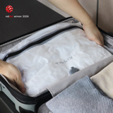 Hands settling a white TILLIV Compak Medium full of folded clothing into an open suitcase