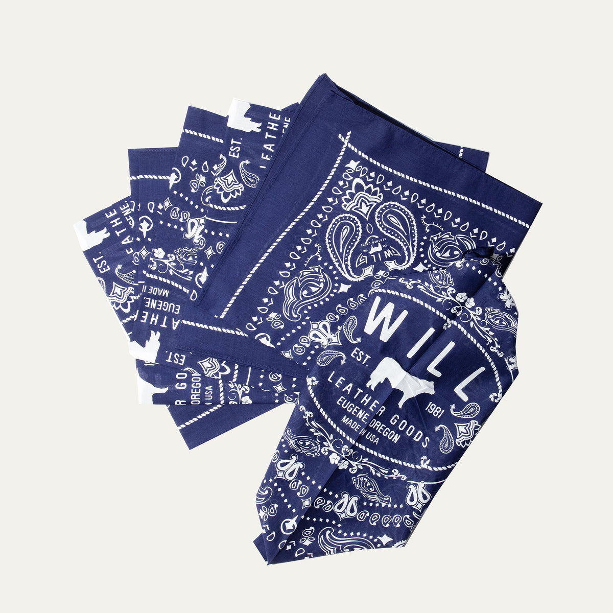 Several navy blue paisley Will's Bandanas fanned out to show the folded stack and logo corner detail.