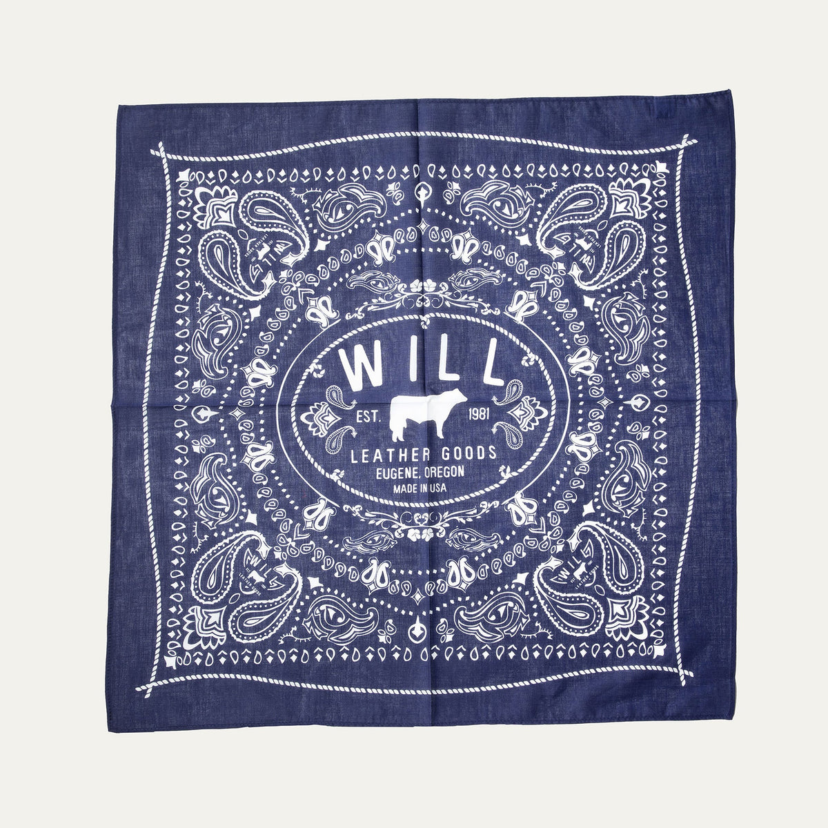 Will's Bandana in navy blue paisley print, laid flat showing the center WILL Leather Goods cattle-brand logo, on a white background.