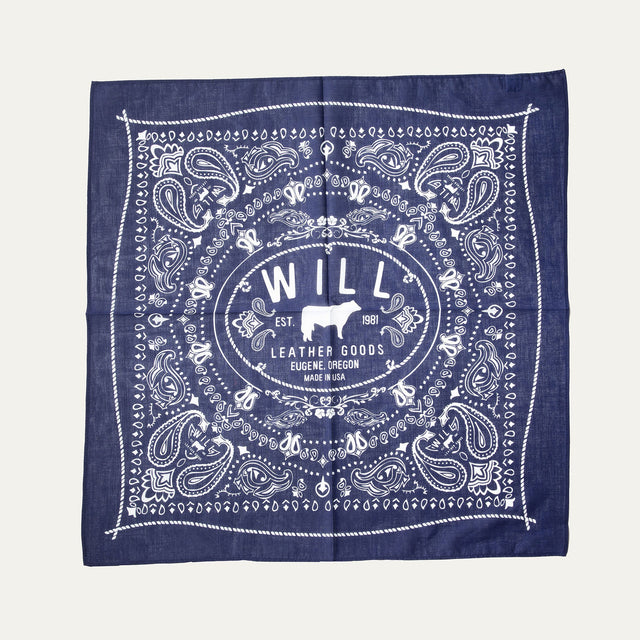 Will's Bandana in navy blue paisley print, laid flat showing the center WILL Leather Goods cattle-brand logo, on a white background.