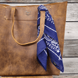Lifestyle photo of the navy paisley Will's Bandana tied around the handle of a brown leather tote bag.