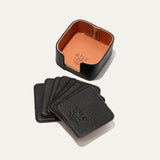 Open round leather holder for the black Set of Eight Coasters showing its tan interior and embossed WILL Leather Goods logo, with all eight black coasters fanned out below on a white background.