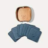 Open round leather holder for the slate blue Set of Eight Coasters showing its tan interior and embossed WILL Leather Goods logo, with all eight blue coasters fanned out below on a white background.