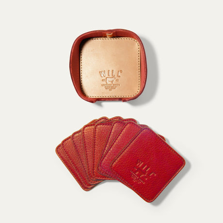 Open round leather holder for the red Set of Eight Coasters showing its tan interior and embossed WILL Leather Goods logo, with all eight red coasters fanned out below on a white background.
