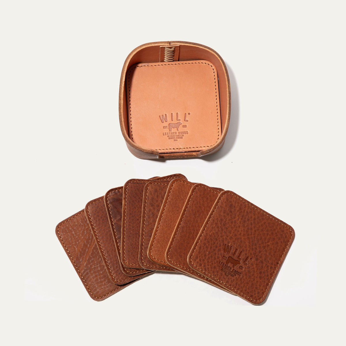 Open round leather holder for the tan Set of Eight Coasters showing its lighter tan interior and embossed WILL Leather Goods logo, with all eight tan coasters fanned out below on a white background.