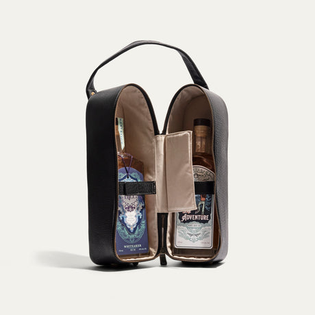 Will Leather Goods Hard Double Leather Wine Case in black leather, unzipped and opened flat to reveal two labeled spirits bottles secured by interior straps.