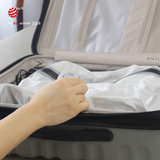 A hand pressing a Nano Pump onto the valve of a white TILLIV Compak Large inside an open suitcase