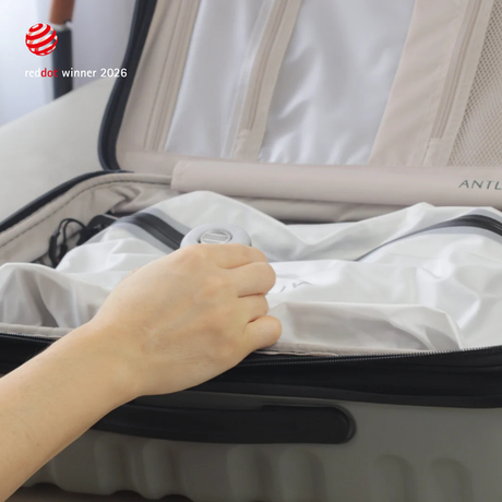 A hand pressing a Nano Pump onto the valve of a white TILLIV Compak Large inside an open suitcase