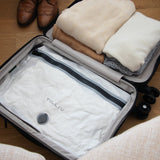 A white TILLIV Compak Large filling the base of an open suitcase, with folded knitwear and brown brogues alongside