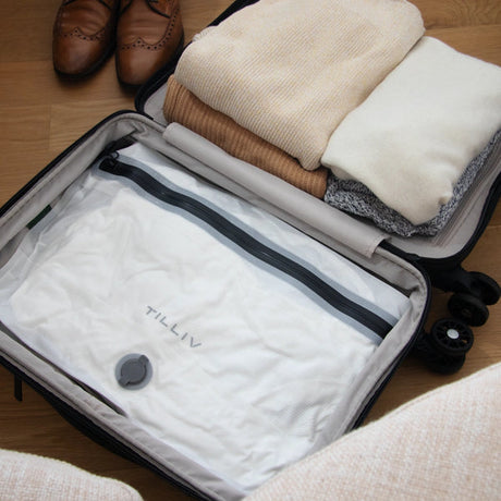 A white TILLIV Compak Large filling the base of an open suitcase, with folded knitwear and brown brogues alongside