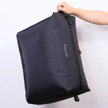 A hand holding a packed Graphite Gray TILLIV Kamper by its corner, showing its soft, flexible shape