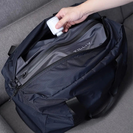A hand holding a TILLIV Nano Pump to the valve of a Kamper vacuum pack fitted inside an open navy duffel bag