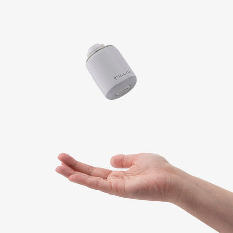 A white TILLIV Nano Pump caught in mid-air above an open palm, showing how light it is