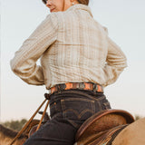 Lifestyle photo of a woman on horseback wearing the tri-color Hand Laced Link Belt over jeans, seen from behind against an open sky.