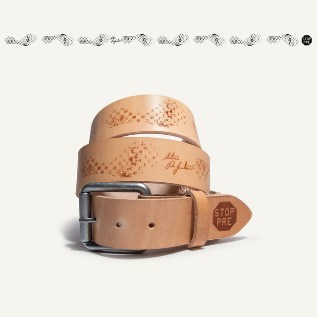 Natural tan leather belt coiled upright, showing the gunmetal roller buckle and brown waffle-tread emboss pattern along the strap, with a STOP PRE tab stamped near the tip