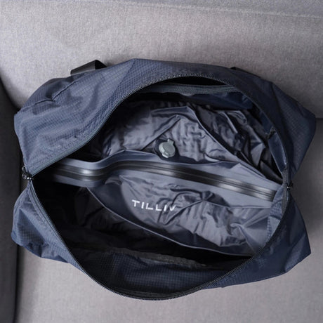 Looking down into an open navy Pakke duffel at the empty grey Kamper vacuum pack anchored across its base, valve visible