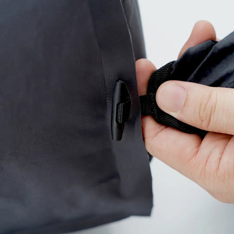 A hand threading a webbing strap through the anchor loop on the side of the TILLIV Kamper vacuum pack