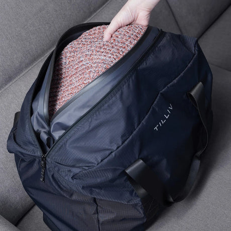 A hand lowering a folded pink and grey knitted jumper into the Kamper vacuum pack inside a navy Pakke duffel