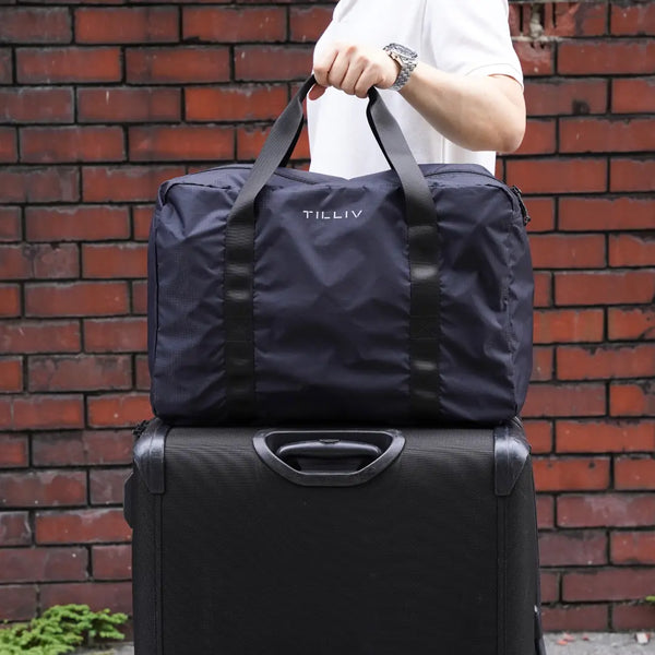 A packed navy TILLIV Pakke duffel resting on top of a black suitcase, held by its handles