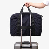 An open navy TILLIV Pakke duffel on a sofa with white trainers packed inside
